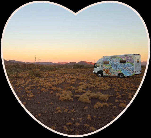 A mobile health van parked in outback scrubland at sunset