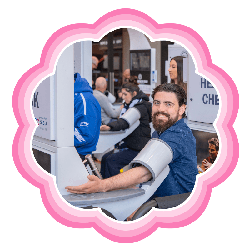 A man smiling as he takes a free blood pressure reading at a Shane Warne Legacy health check station in a shopping centre